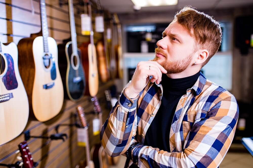 homem bonito escolhendo um violão em uma loja de música