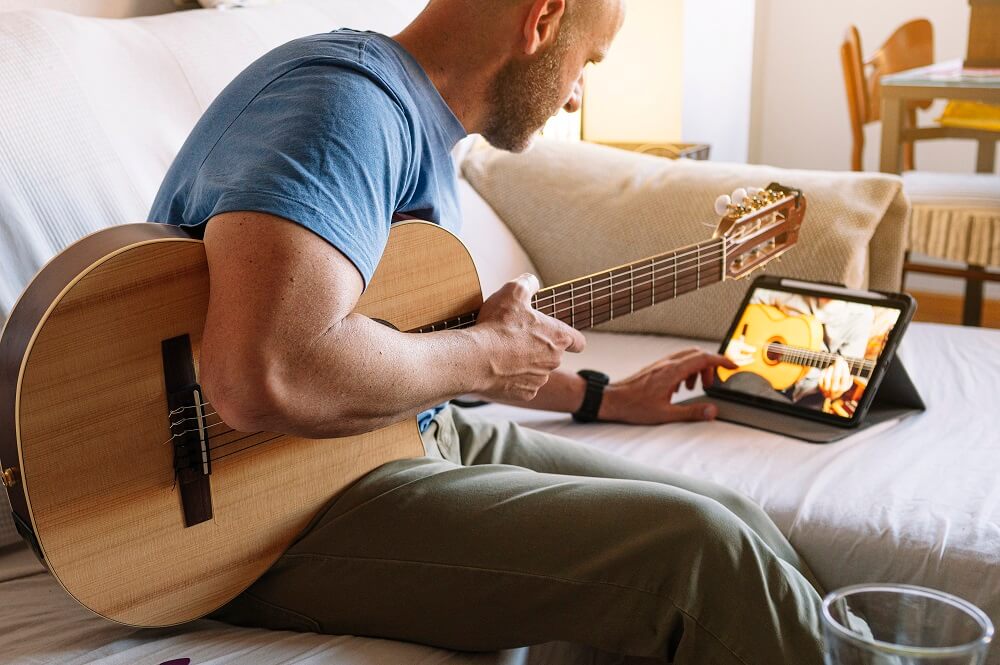 Homem adulto estudando violão online com tablet em casa
