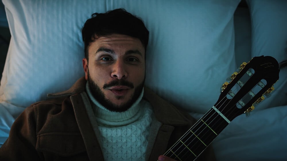 homem tocando violão deitado na cama